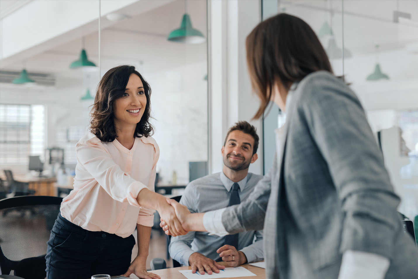Two women shaking hands while a man looks on